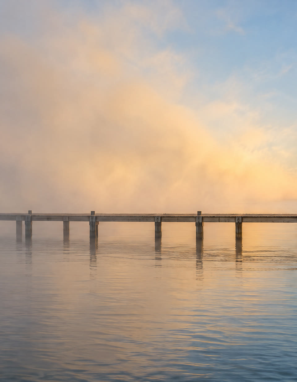 The same pier as the fog thins and glows gold in the rising sun.