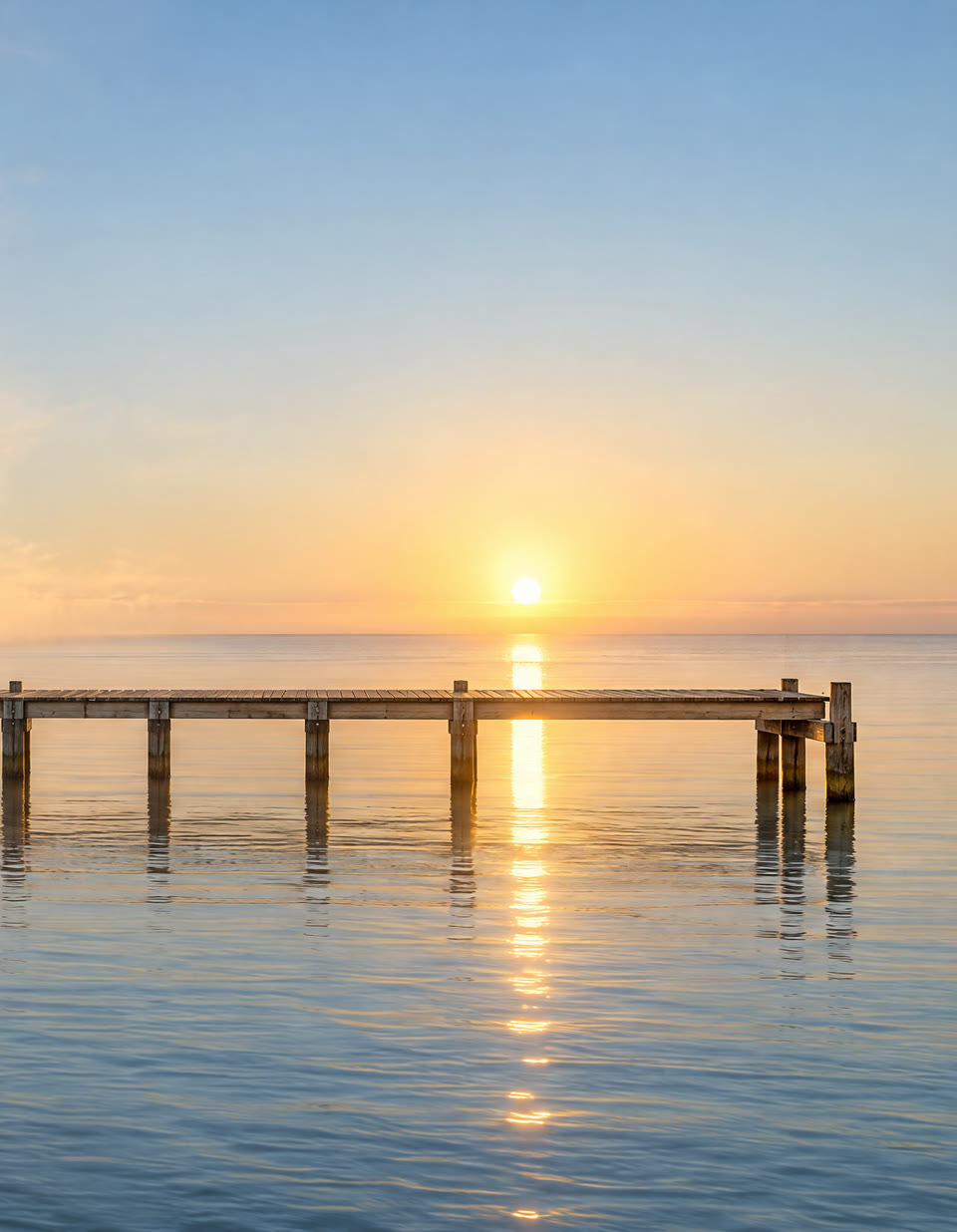 The end of the pier in clear air, with the sun rising over a calm sea.